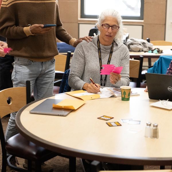 A woman writing notes while a man stands beside her holding pink cards.