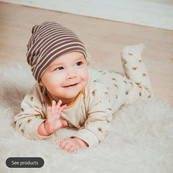 Smiling baby in pajamas and striped hat lying on a fluffy rug.