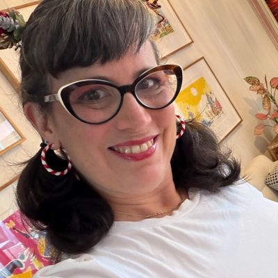 Woman with cat-eye glasses and candy cane earrings smiling indoors.