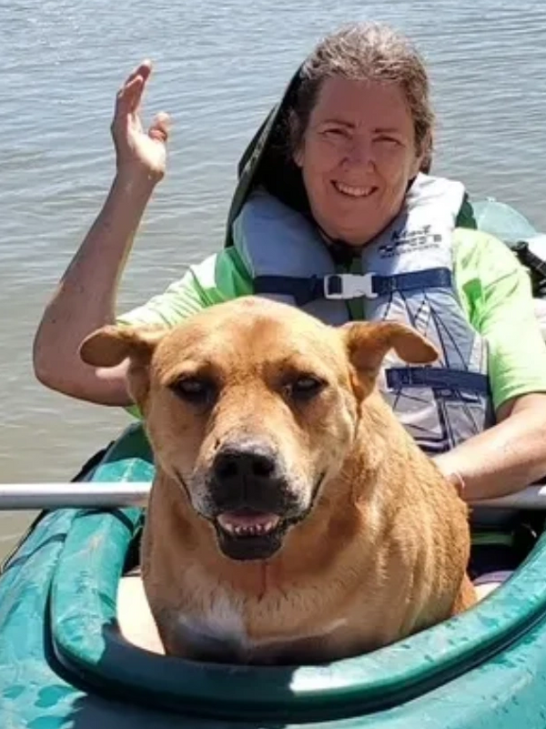 A woman and her dog enjoy a sunny day kayaking on calm water.