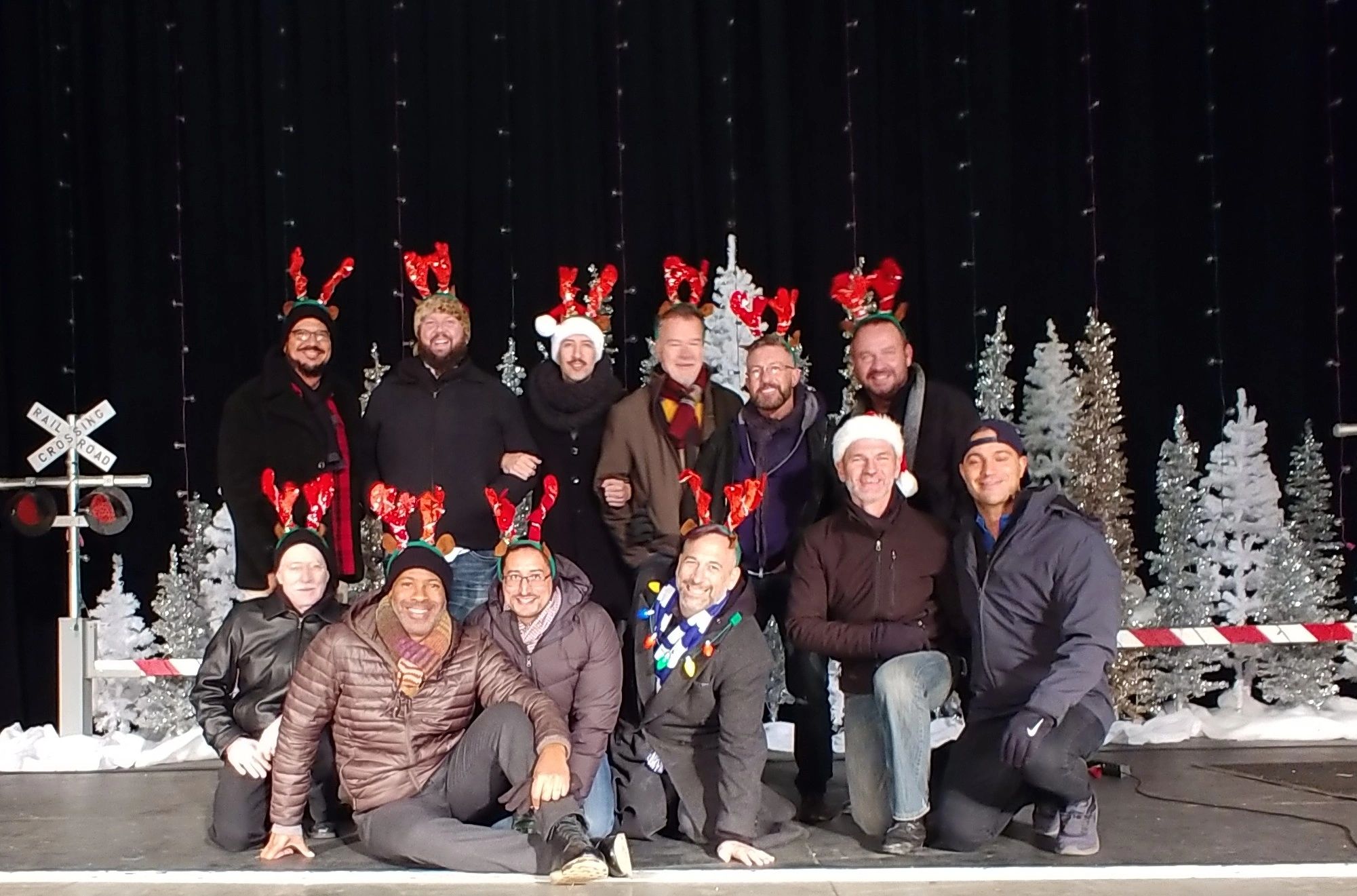 Group of men in festive antler headbands posing in front of holiday decorations.