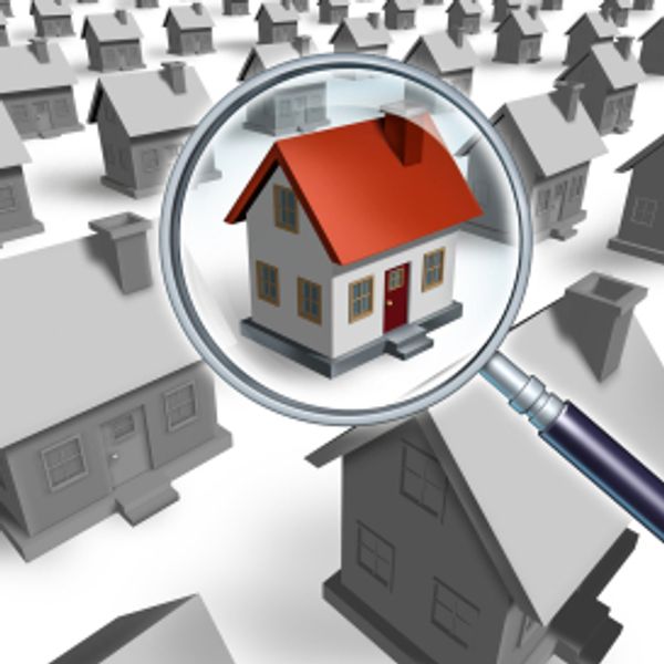 A magnifying glass highlighting a house with a red roof among many gray houses.