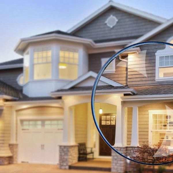 Hand holding magnifying glass focusing on a house's front porch at dusk.