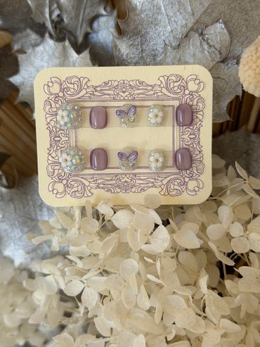 Elegant purple and glittery press-on nails with floral and butterfly designs.