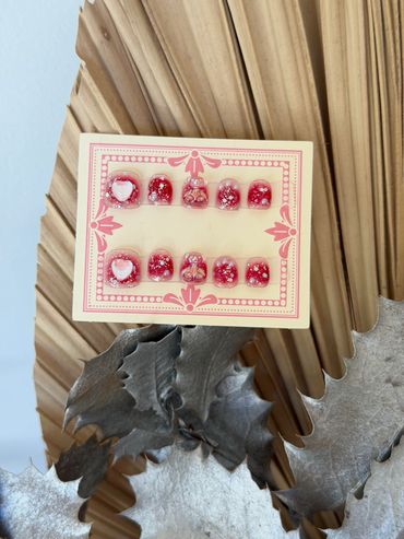 Set of decorative red and white press-on nails with heart and glitter designs.