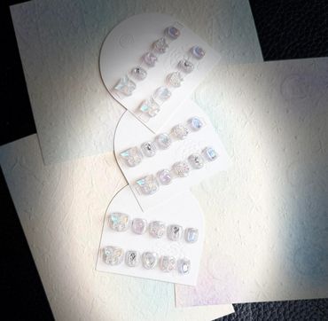 Elegant iridescent nail art sets displayed on white cards with a textured background.