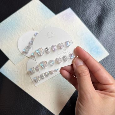 Hand holding a card with shiny decorative nail art pieces.