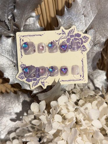 Elegant purple nail art set with gemstone accents on a decorative card.