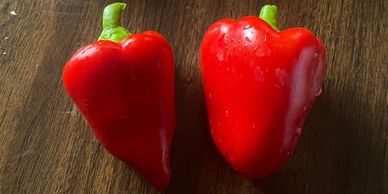 Two fresh red bell peppers with green stems on a wooden surface.