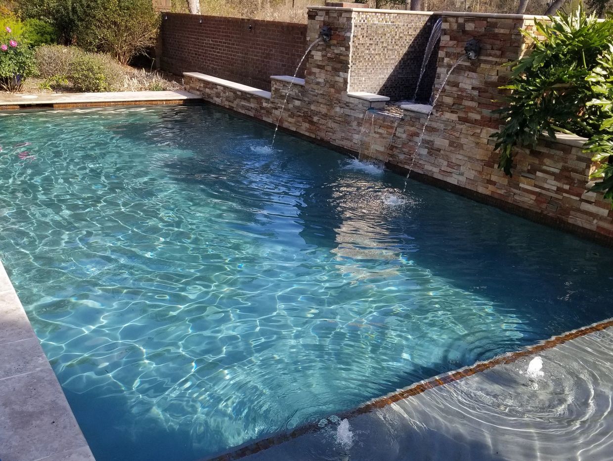 Clear blue pool with decorative water fountains on a stone wall.