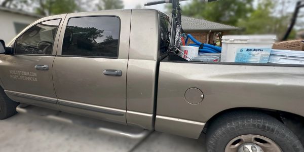 Pickup truck loaded with pool service equipment parked outside.