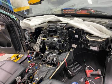 Car interior with dashboard removed and tools scattered.