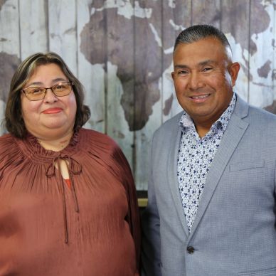 Two smiling individuals posing indoors with a world map backdrop.