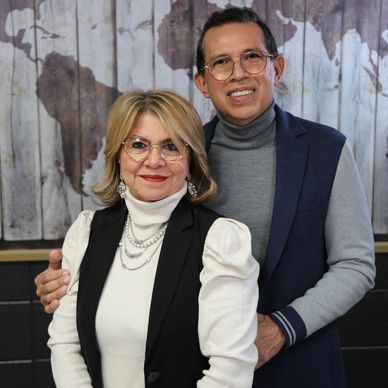 A smiling man and woman posing together indoors in front of a world map.