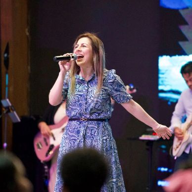 Woman passionately singing on stage with band in background.