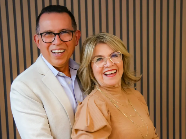 Smiling couple wearing glasses posing against striped wooden wall.