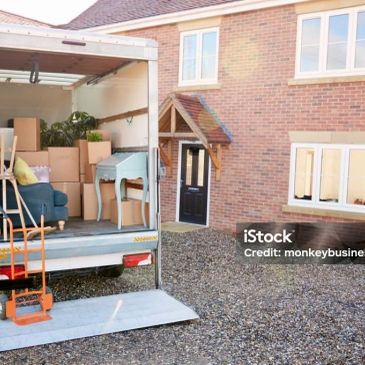 Moving boxes and furniture loaded in a truck outside a house.