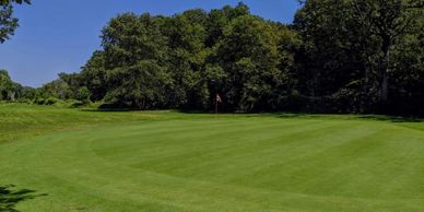 A lush green golf course with a flagstick on the putting green.
