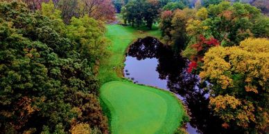 A golf course surrounded by colorful autumn trees and a water hazard.