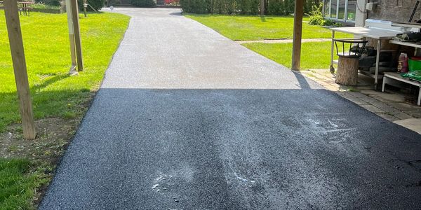 Newly paved black asphalt driveway leading to a lighter concrete path.