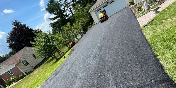 Freshly paved asphalt driveway leading to a white garage on a sunny day.