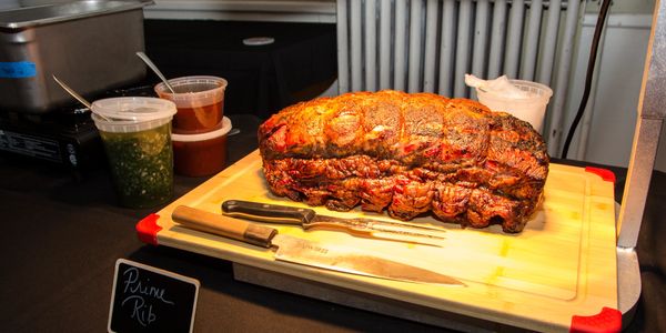 A cooked prime rib on a cutting board with knives and sauces.