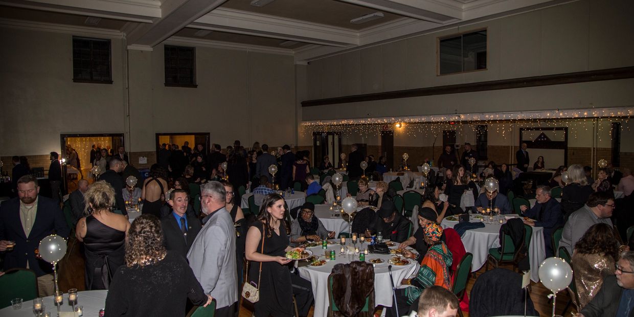 Guests enjoy a formal dinner party in a decorated hall with balloons and fairy lights.