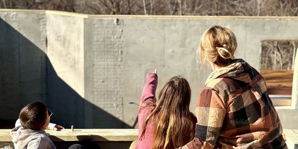 A woman and two children looking at a construction site under clear sky.