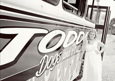 A bride leaning against the original Todd's Dogs food truck pictured in black and white