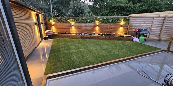 Modern backyard with grass, tiled patio, wooden fence, and ambient lighting.