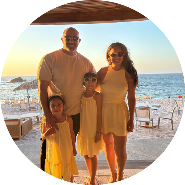 Family of four dressed in yellow, posing at a beachside restaurant during sunset.