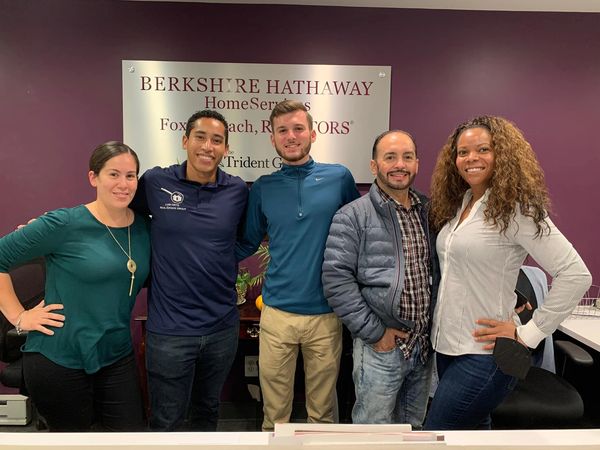 A diverse group of five people standing together smiling inside a Berkshire Hathaway office.