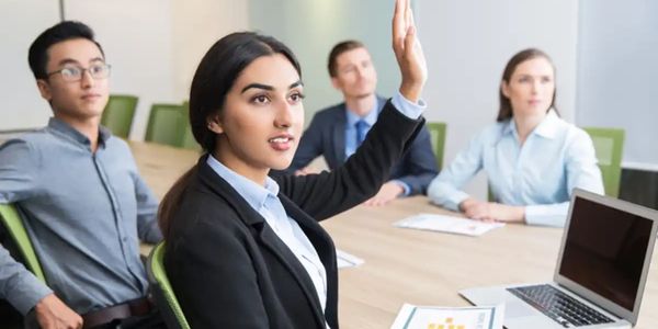 Trainees sitting at a table. One trainee raises hand for question