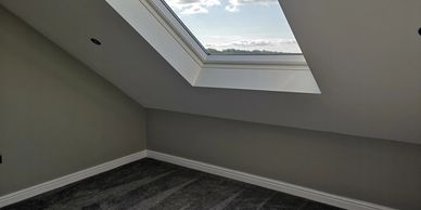 Empty room corner with a skylight window and gray carpet.