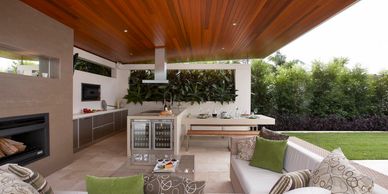 Modern outdoor kitchen and lounge area with wooden ceiling and green accents.