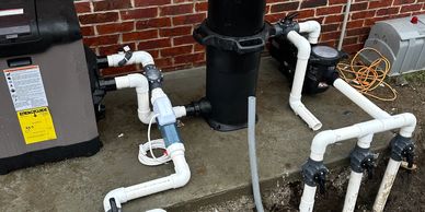 Outdoor pool pump and filtration system setup against a brick wall.