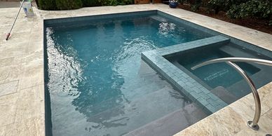 Modern backyard pool with clear blue water and beige stone tiles.