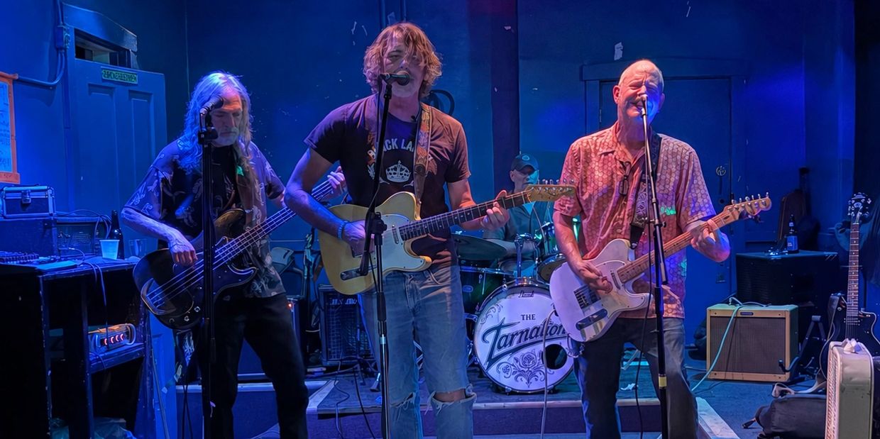 Band performing live on stage with guitars and drums.