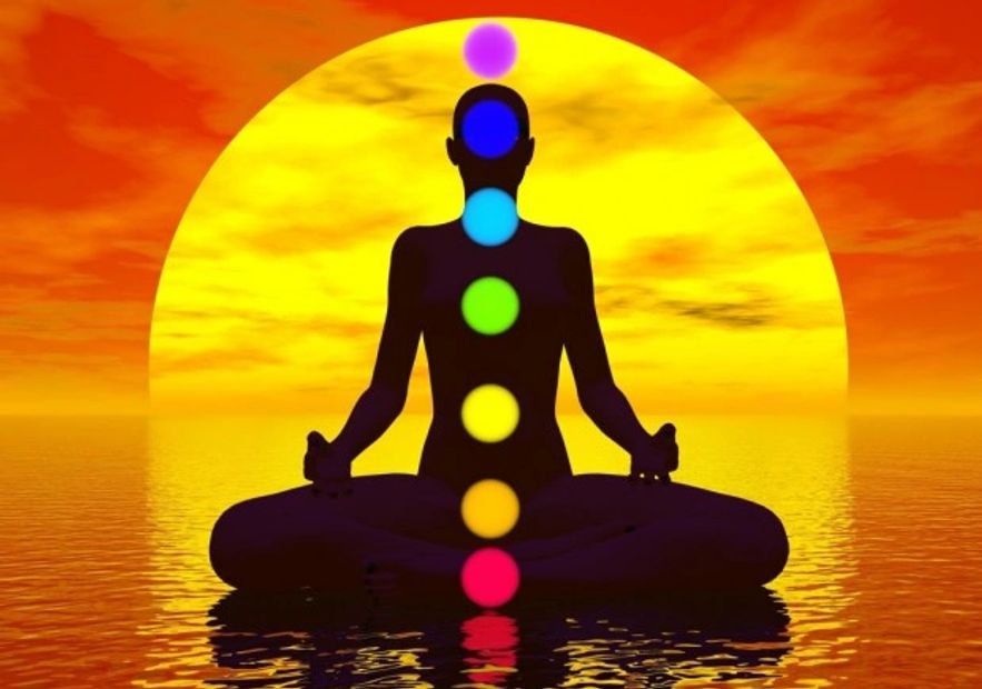 Person seated on water in lotus position with chakra orbs aligned in the body vertically and the sunset behind them