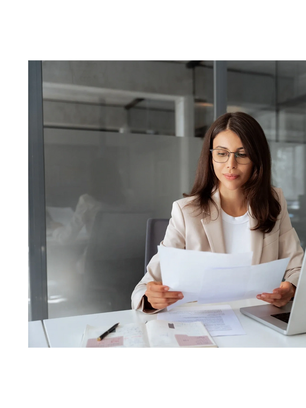 Professional woman reviewing documents at her office desk with a laptop.