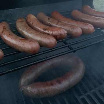 Sausages grilling on a barbecue grill with smoke rising.