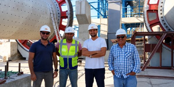 Vier bouwvakkers poseren bij een fabriek met helmen op.