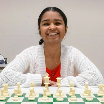 Smiling girl sitting behind a chessboard.