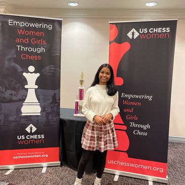 Woman standing between two US Chess Women banners.