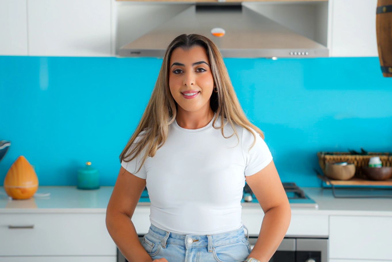 Smiling woman standing confidently in a modern kitchen with blue backsplash.