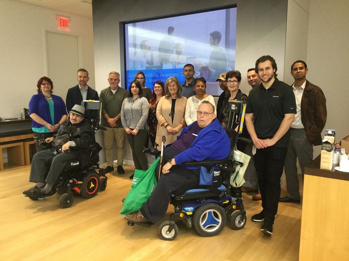 16 adults with the two men in the front in wheelchairs, the remainder of people are standing. 