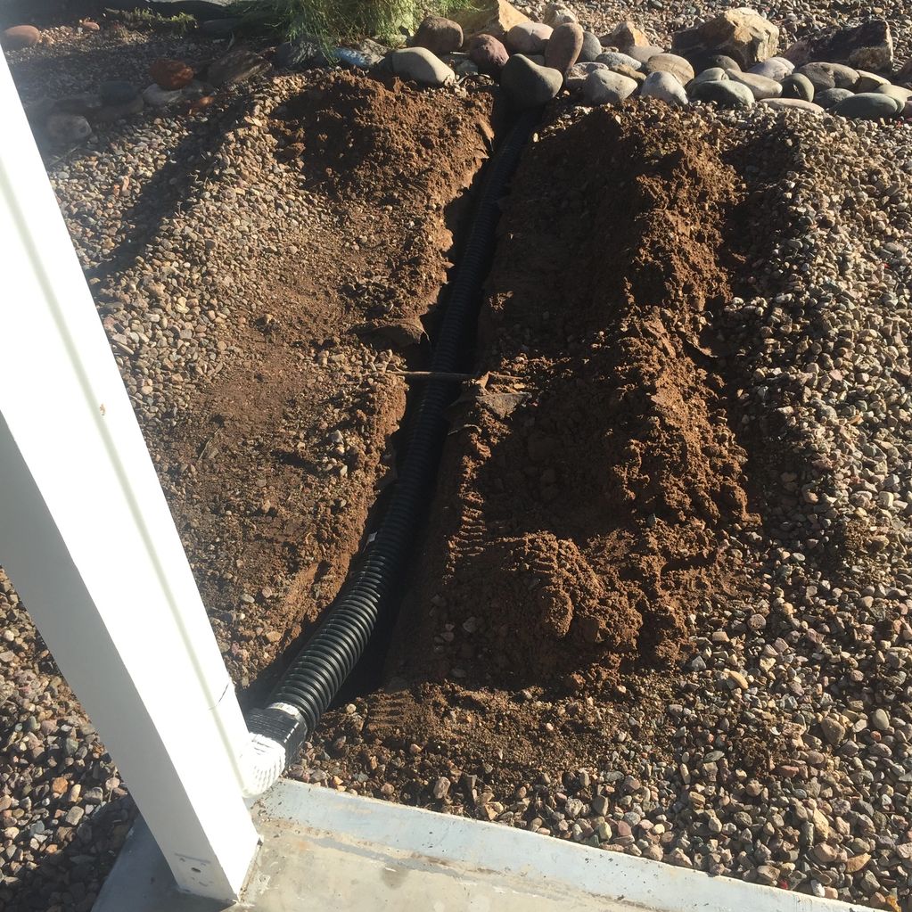 A black drainage pipe installed in a trench surrounded by rocks and dirt.