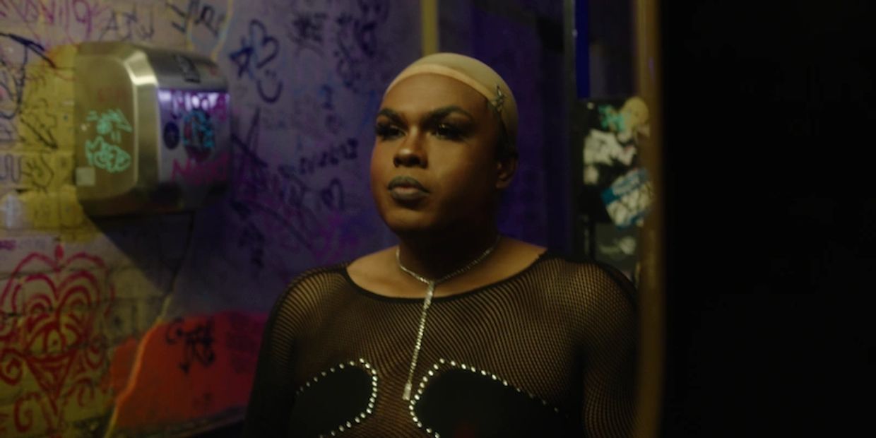 Person wearing a netted top and makeup in a graffiti-covered room.