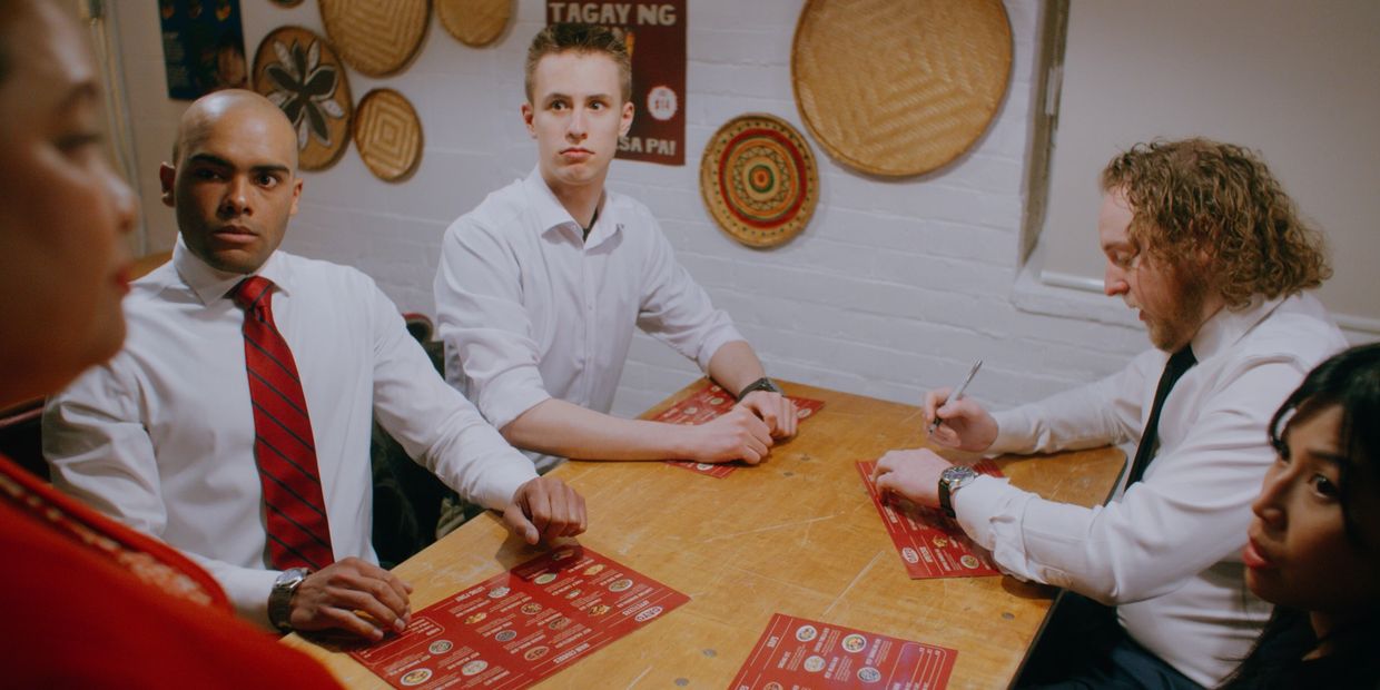 Four people in white shirts and ties sitting around a wooden table with menus.