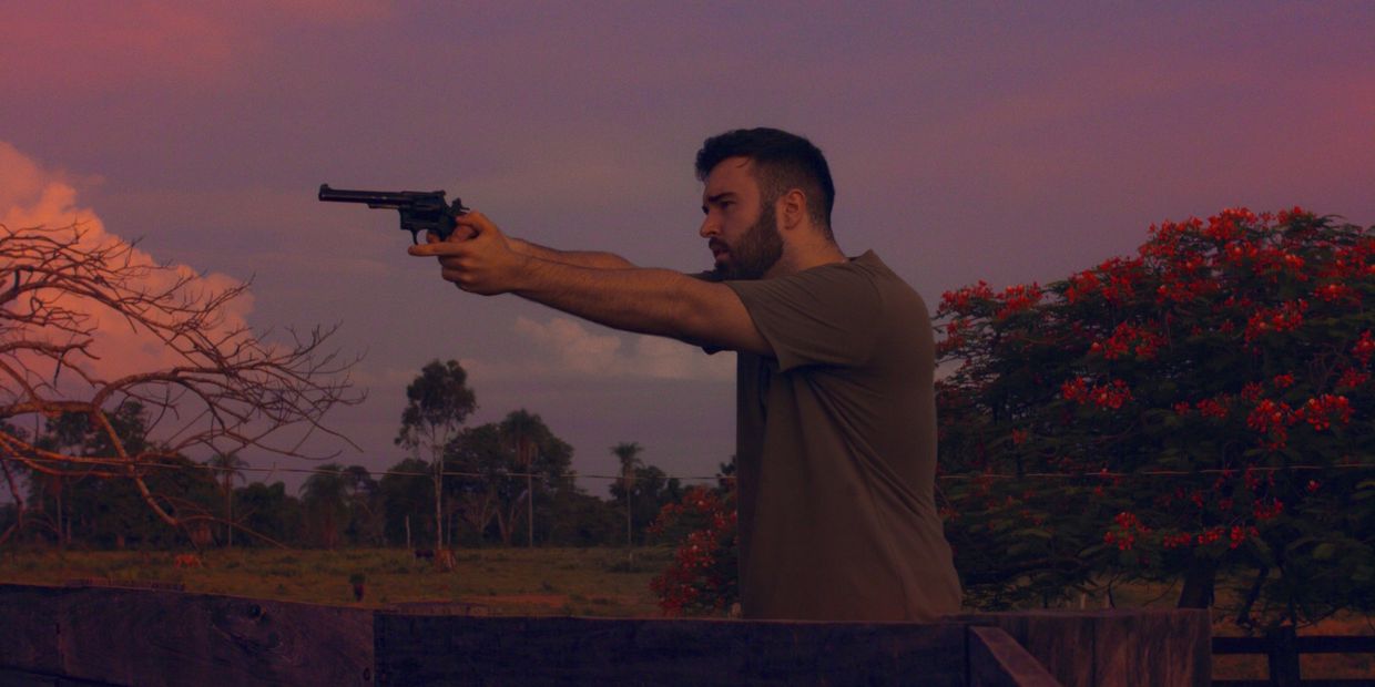 Man aiming a revolver in an outdoor setting at dusk.